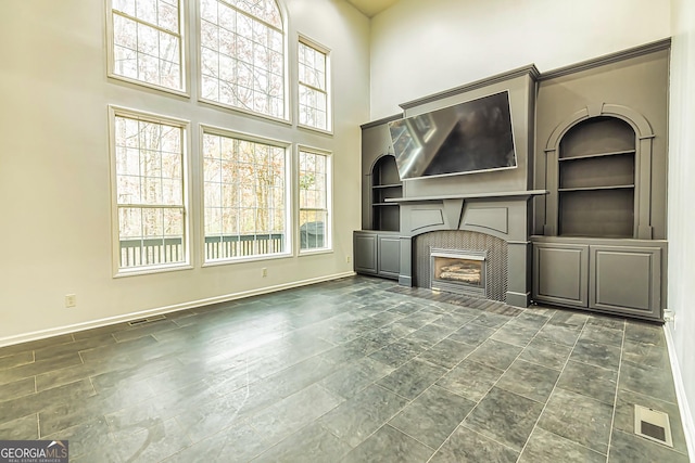 unfurnished living room with a fireplace, built in features, and a towering ceiling