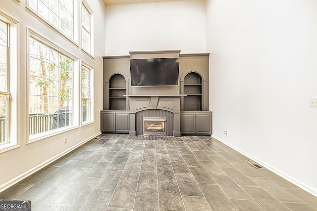 unfurnished living room featuring built in shelves, a high ceiling, and a brick fireplace