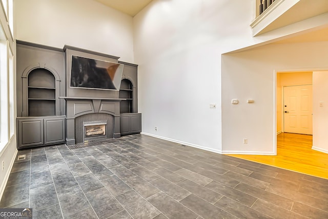 unfurnished living room featuring a high ceiling, built in features, and dark wood-type flooring