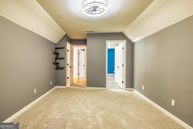 additional living space featuring lofted ceiling, a textured ceiling, and light carpet