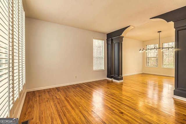 unfurnished living room with a notable chandelier, wood-type flooring, and ornate columns