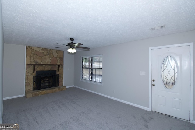 carpeted foyer entrance with a textured ceiling, a stone fireplace, and ceiling fan