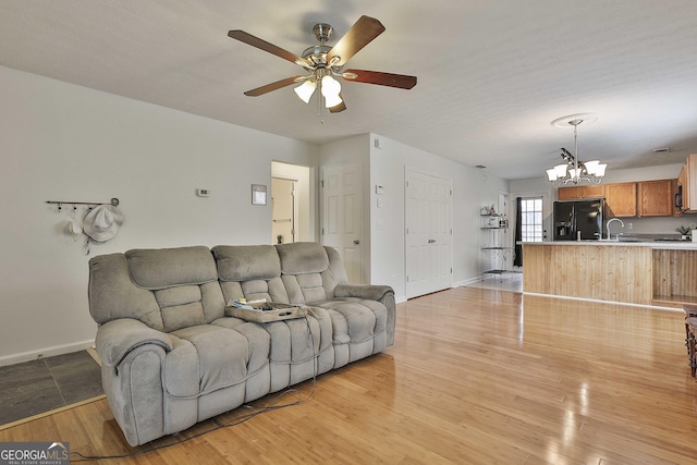 living room featuring ceiling fan with notable chandelier, sink, and light hardwood / wood-style flooring