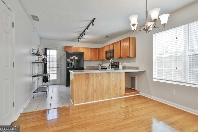 kitchen with kitchen peninsula, light wood-type flooring, sink, black appliances, and a chandelier