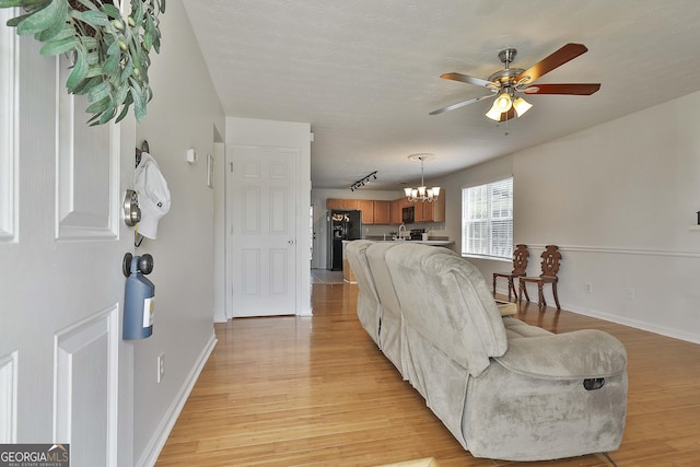 living room featuring ceiling fan with notable chandelier and light wood-type flooring