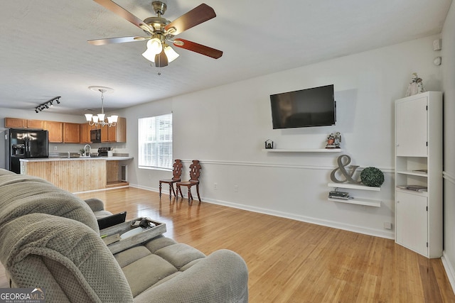 living room with ceiling fan with notable chandelier, light wood-type flooring, and sink