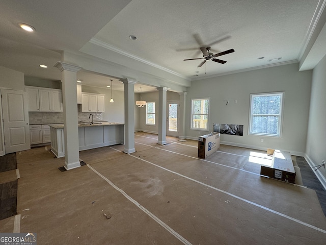 unfurnished living room with crown molding, a healthy amount of sunlight, decorative columns, and baseboards