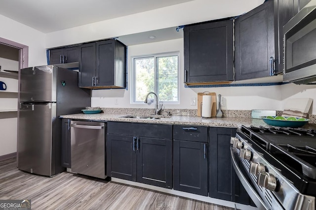 kitchen with appliances with stainless steel finishes, light stone counters, light hardwood / wood-style flooring, and sink