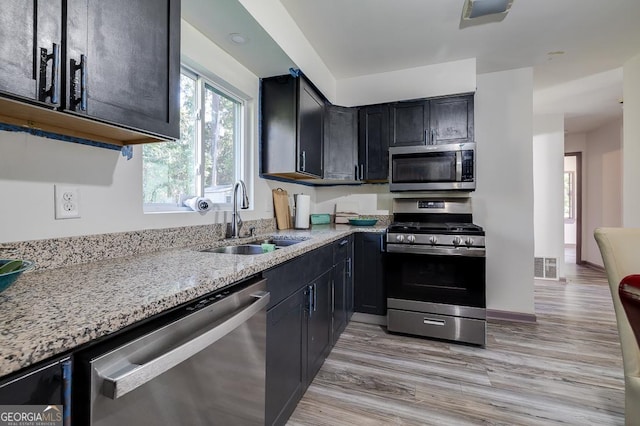 kitchen with sink, light stone countertops, stainless steel appliances, and light hardwood / wood-style flooring