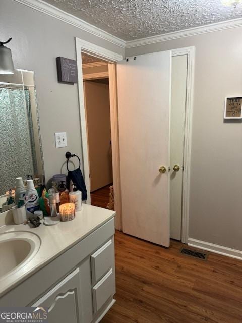 bathroom with vanity, a textured ceiling, hardwood / wood-style flooring, and crown molding