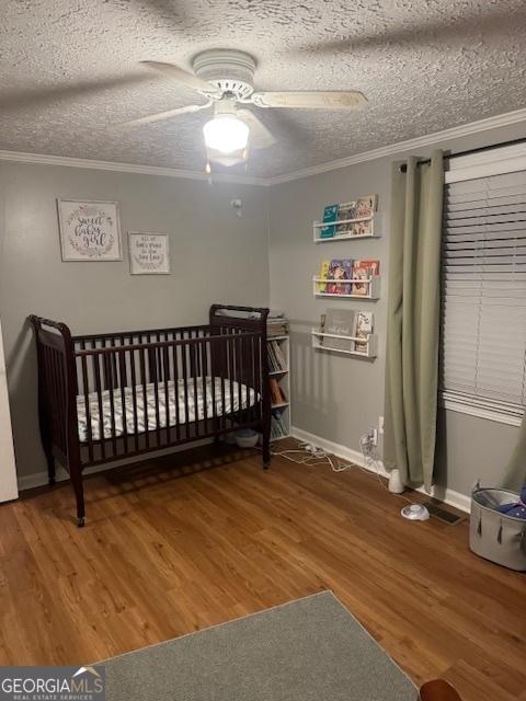 bedroom featuring ceiling fan, crown molding, wood-type flooring, a textured ceiling, and a nursery area