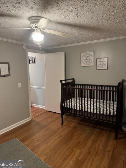 bedroom featuring ceiling fan, hardwood / wood-style floors, a nursery area, and a textured ceiling