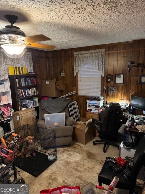 carpeted office space featuring wood walls, ceiling fan, and a textured ceiling