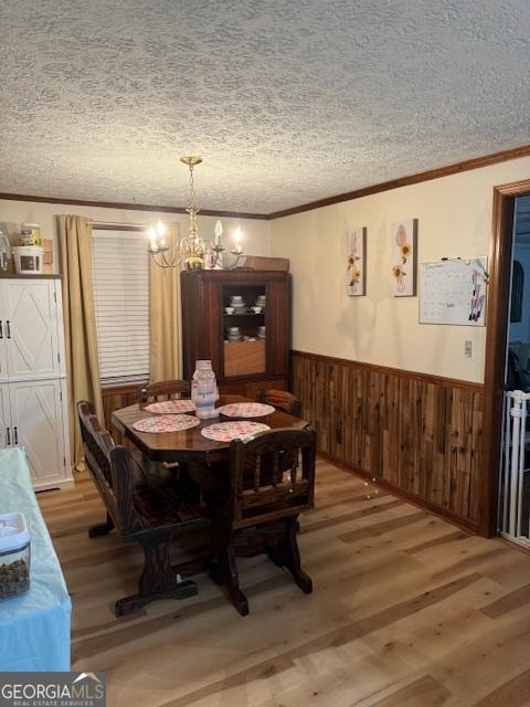 dining room with hardwood / wood-style floors, a textured ceiling, an inviting chandelier, and ornamental molding