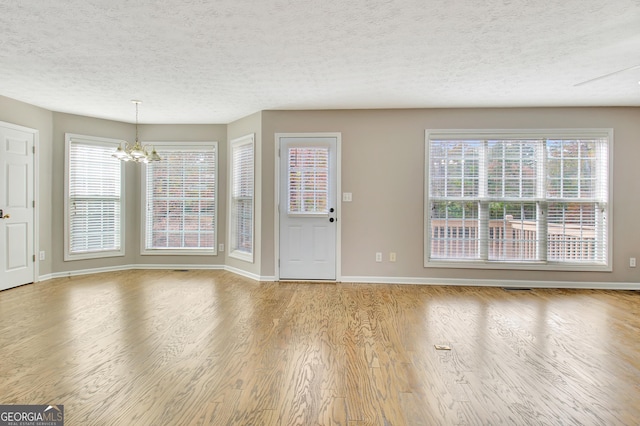 entrance foyer with baseboards, a textured ceiling, an inviting chandelier, and wood finished floors