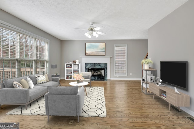 living room featuring a premium fireplace, ceiling fan, a textured ceiling, wood finished floors, and baseboards