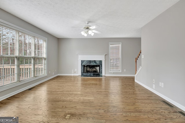 unfurnished living room with a fireplace, visible vents, stairway, ceiling fan, and wood finished floors