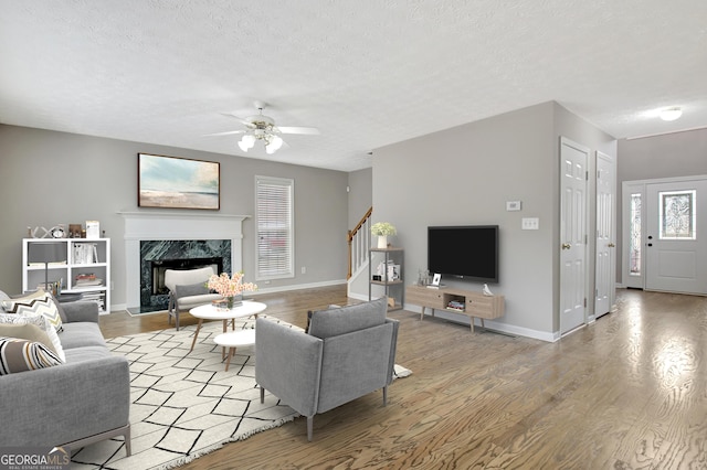 living area with a textured ceiling, a fireplace, wood finished floors, a ceiling fan, and stairway