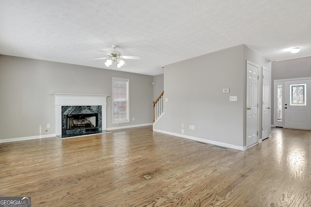 unfurnished living room featuring stairs, a premium fireplace, wood finished floors, and a textured ceiling