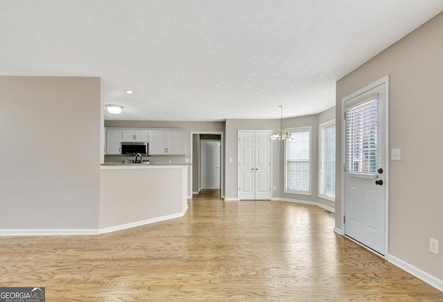 unfurnished living room with light wood-type flooring, a notable chandelier, a textured ceiling, and baseboards