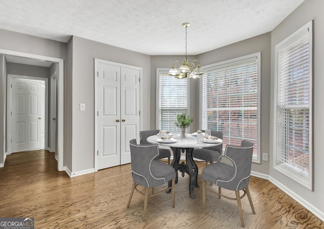 dining space featuring a notable chandelier, a textured ceiling, baseboards, and wood finished floors