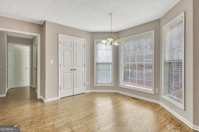 unfurnished dining area with baseboards, visible vents, an inviting chandelier, a textured ceiling, and light wood-type flooring