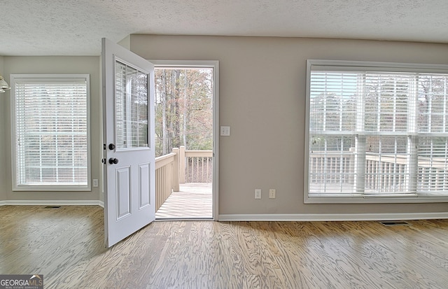 doorway to outside with visible vents, a textured ceiling, baseboards, and wood finished floors