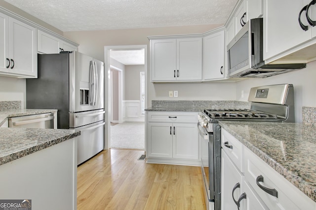 kitchen featuring light stone countertops, wainscoting, appliances with stainless steel finishes, white cabinets, and light wood-type flooring