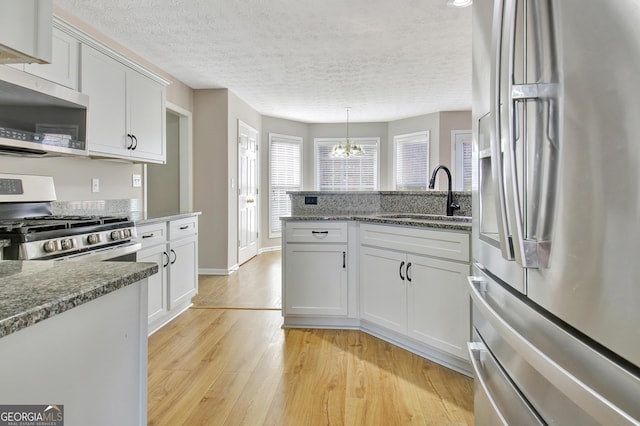 kitchen featuring white cabinets, a sink, appliances with stainless steel finishes, a chandelier, and a peninsula