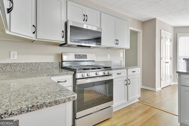 kitchen featuring a textured ceiling, stainless steel appliances, baseboards, light wood-style floors, and light stone countertops