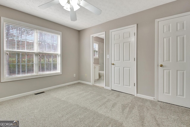 unfurnished bedroom with a textured ceiling, multiple windows, carpet flooring, and visible vents