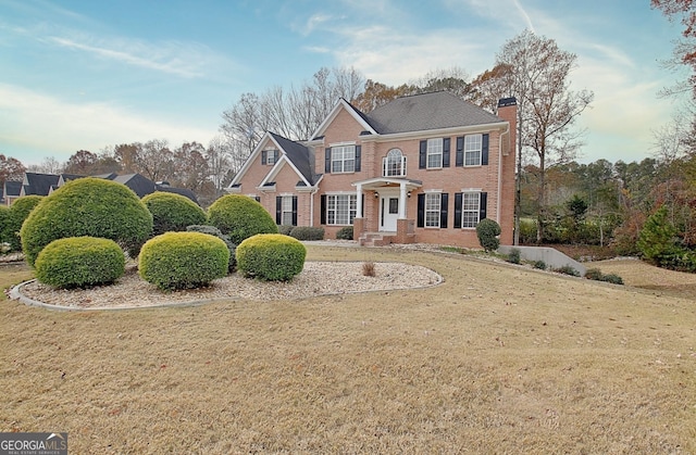 view of front of home with brick siding, a chimney, and a front yard