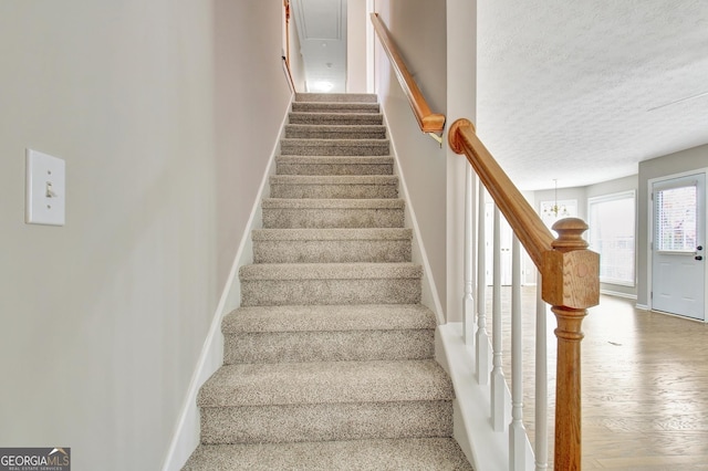 staircase with a textured ceiling, wood finished floors, and baseboards