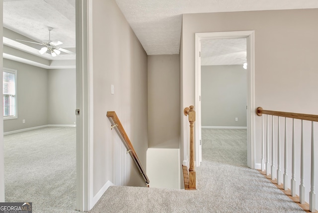 hall featuring a raised ceiling, carpet flooring, a textured ceiling, an upstairs landing, and baseboards