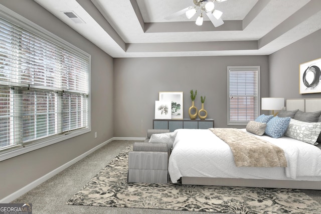 carpeted bedroom featuring baseboards, visible vents, a raised ceiling, and a ceiling fan