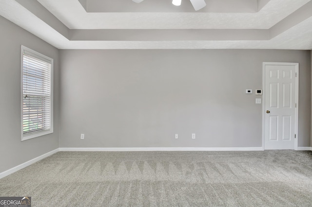 spare room featuring carpet, a raised ceiling, a ceiling fan, and baseboards