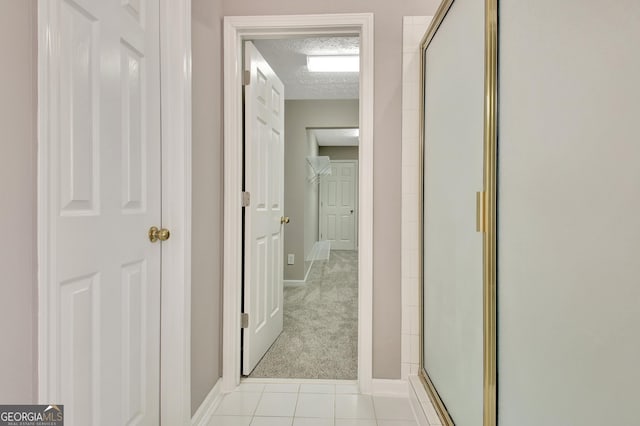 hallway featuring light carpet, baseboards, a textured ceiling, and light tile patterned flooring