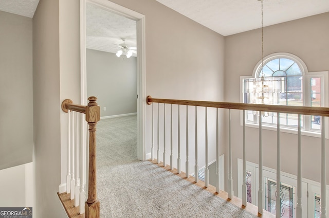 hallway featuring a textured ceiling, carpet, an upstairs landing, and baseboards