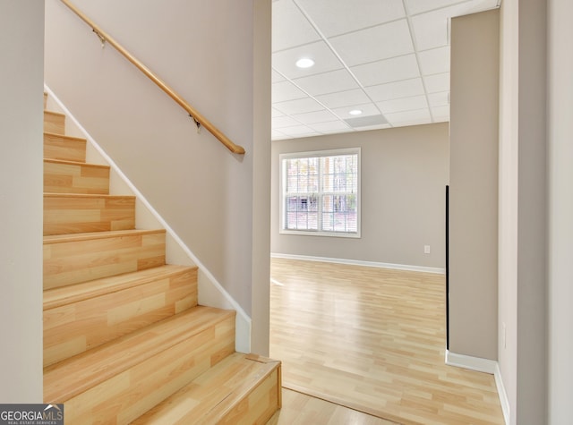 staircase with recessed lighting, a drop ceiling, baseboards, and wood finished floors