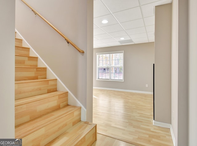 stairs with wood finished floors, recessed lighting, a drop ceiling, and baseboards