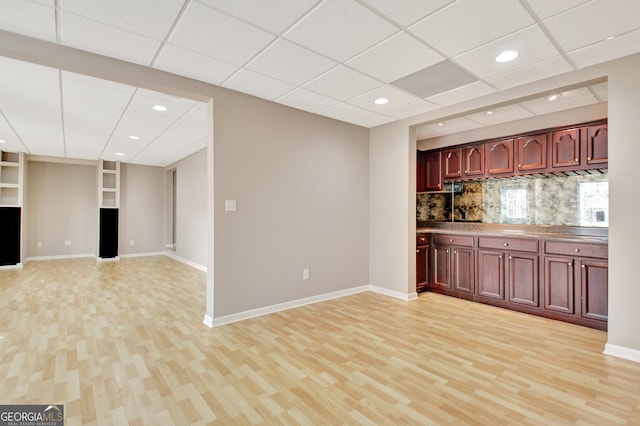 kitchen featuring light wood finished floors, baseboards, decorative backsplash, open floor plan, and dark brown cabinets