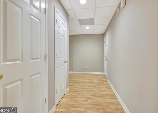 hall featuring baseboards, recessed lighting, a drop ceiling, and light wood-style floors