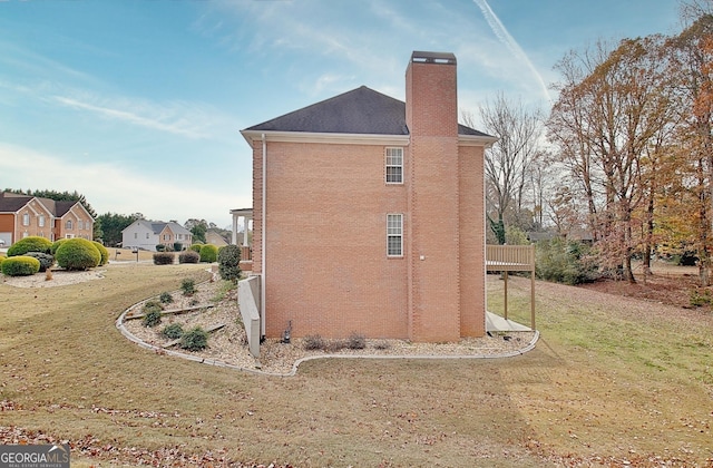 view of home's exterior featuring a chimney, brick siding, a wooden deck, and a yard