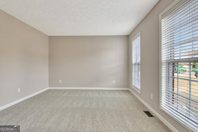 empty room with a textured ceiling, carpet floors, visible vents, and baseboards