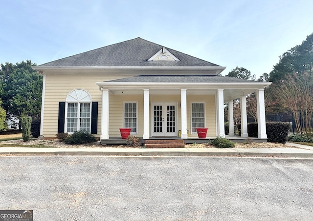 view of front facade with covered porch, french doors, and roof with shingles