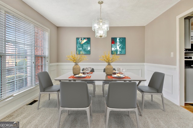 dining space with a wainscoted wall, a notable chandelier, visible vents, and a textured ceiling