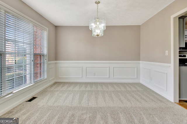 spare room featuring light carpet, visible vents, a chandelier, and a textured ceiling