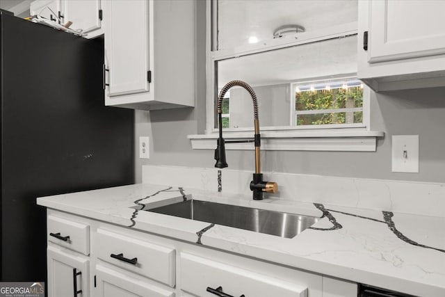 kitchen with white cabinets, black fridge, light stone countertops, and sink