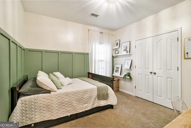 bedroom with a wainscoted wall, a closet, visible vents, a decorative wall, and light carpet