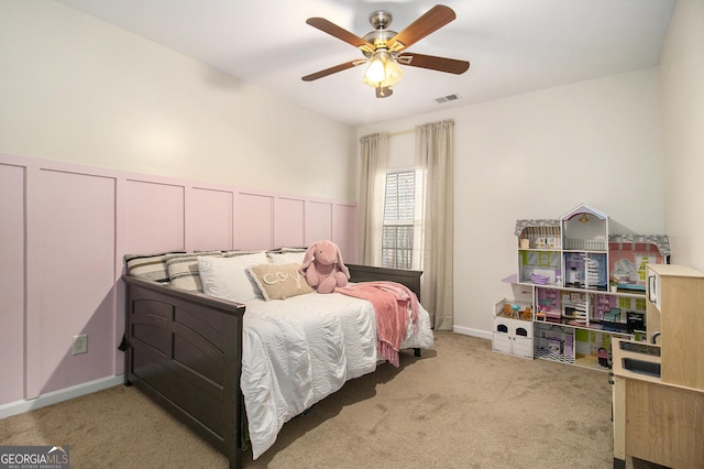 bedroom with light carpet, visible vents, wainscoting, ceiling fan, and a decorative wall